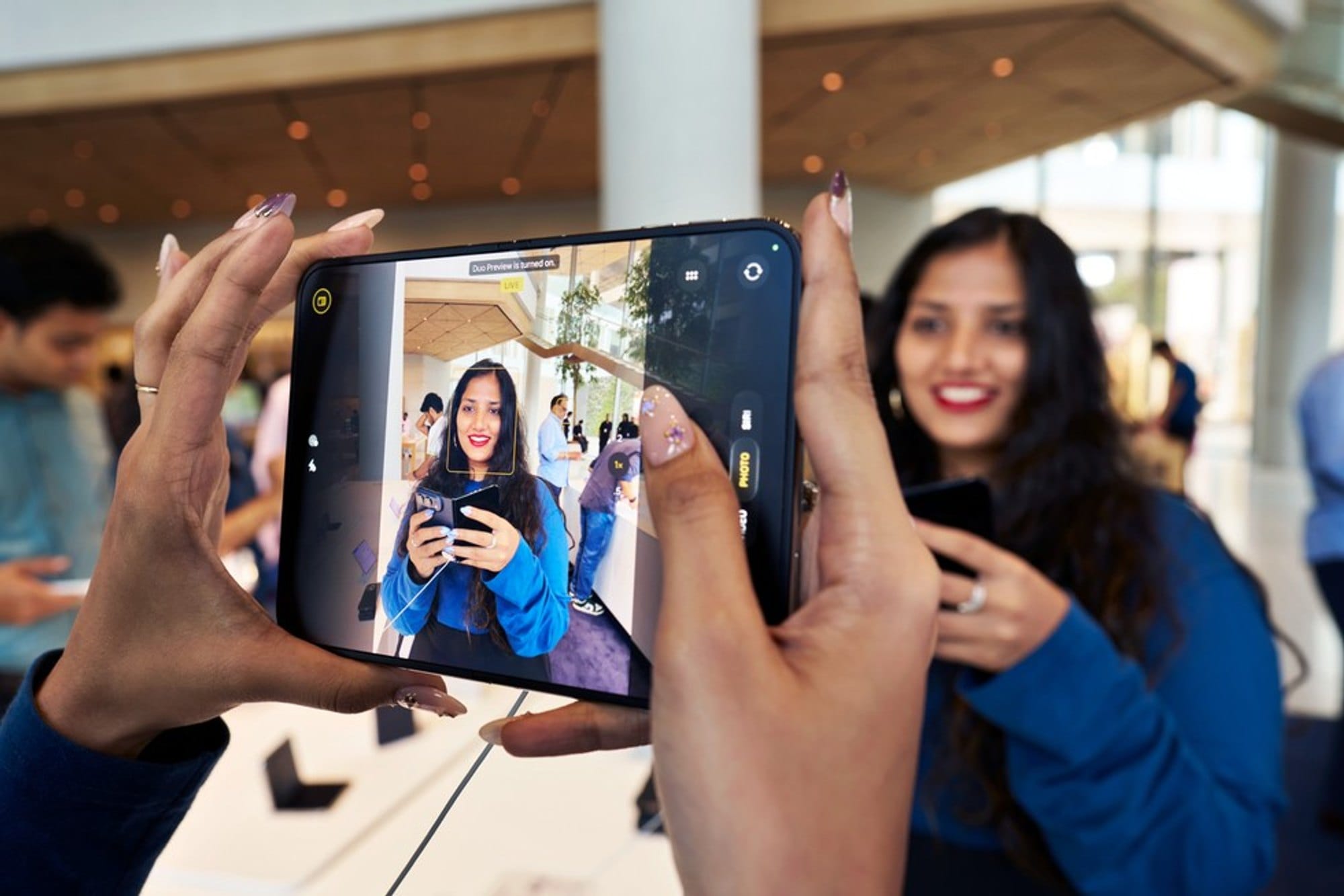A person uses an iPhone Duo to take a photo of another person in an Apple Store