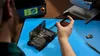 A technician works on an open iPhone held in Apple's repair tray, with a repair press in the background