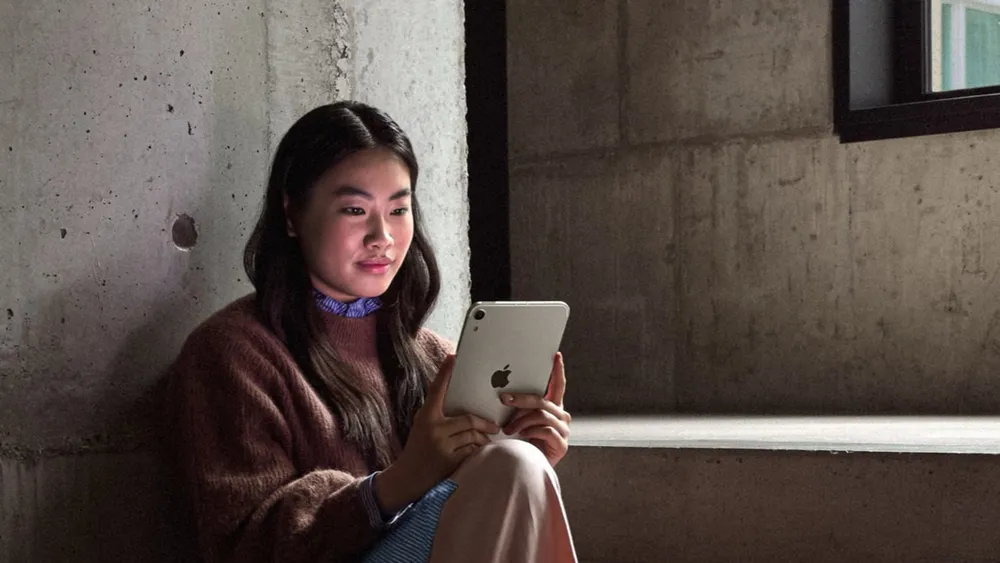 A person sitting by a window reading on the new iPad mini